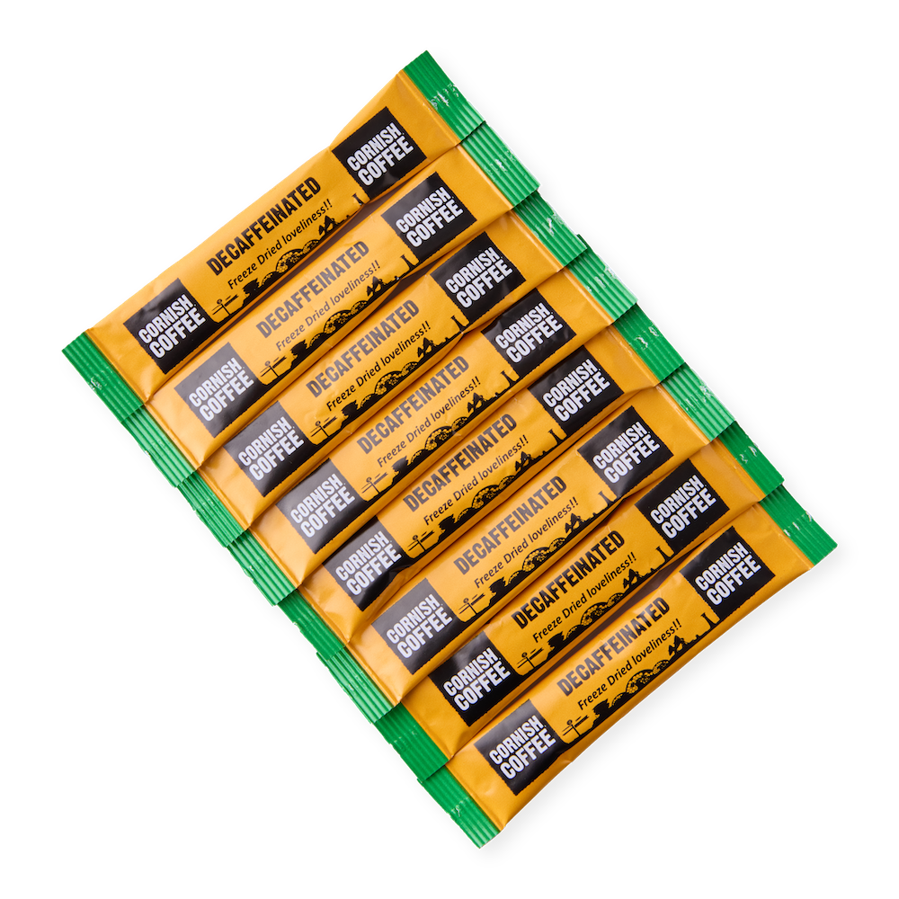 Close-up of Cornish Coffee Decaffeinated Instant Sticks, individually wrapped in yellow and green packaging with “Freeze Dried loveliness!!” printed on each stick.